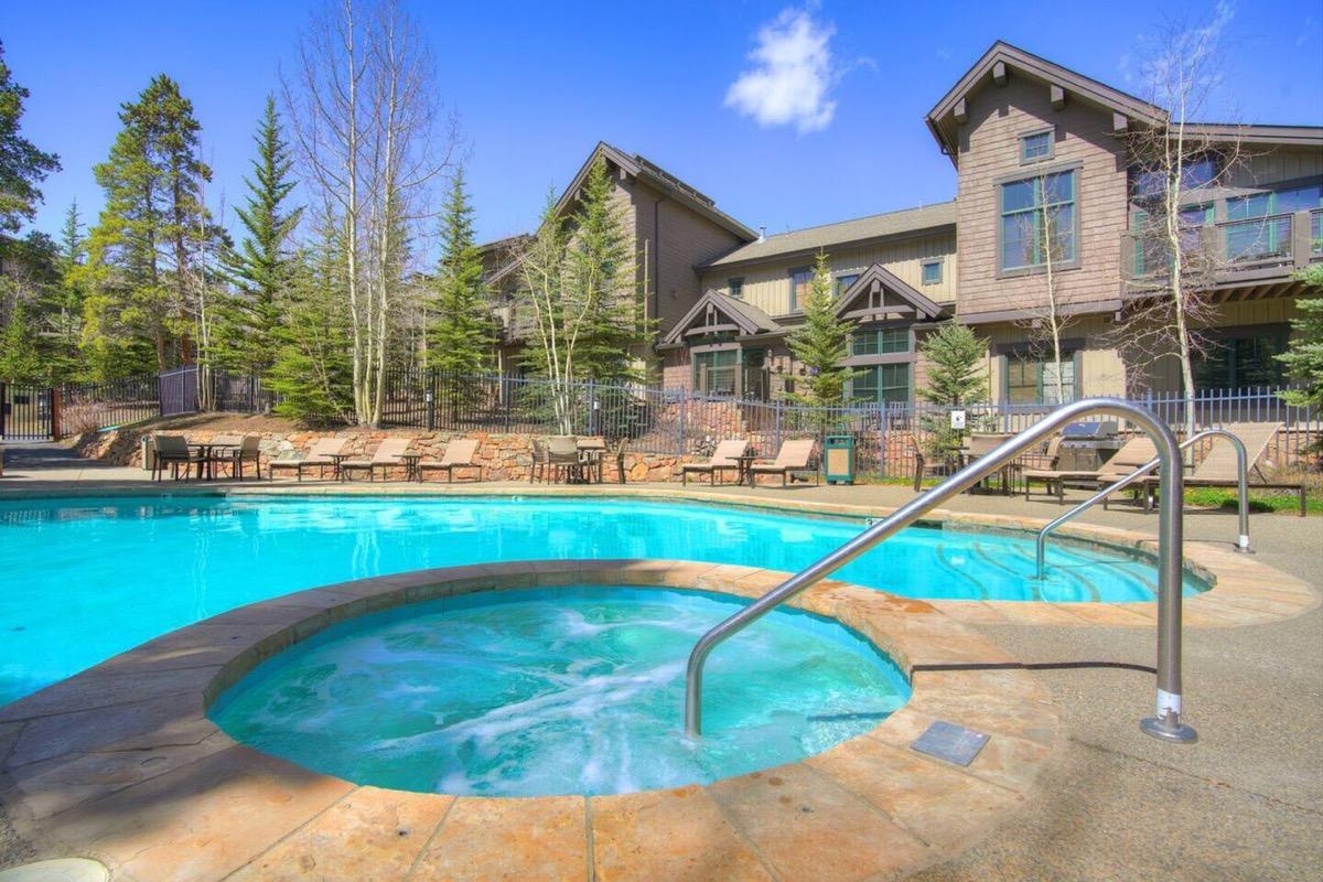 The pool and hot tub deck at Mountain Thunder Lodge in summer, enclosed by lodge buildings and pines
